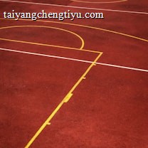 A sports court with a reddish-brown surface and bright yellow and white lines. The lines form geometric shapes, including rectangles and circles, suggesting markings for games like basketball or netball.