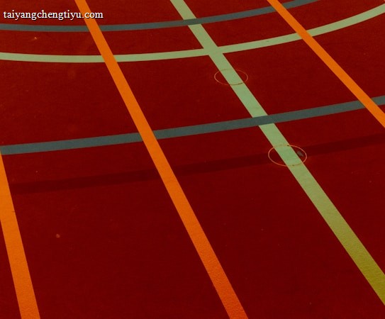 A sports court with intersecting lines in orange and blue, creating geometric patterns on a reddish-brown surface.